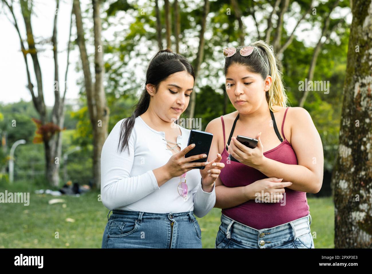 ragazza che mostra alla sua amica i messaggi di testo che ha sul suo telefono cellulare mentre fa una passeggiata nel parco. Foto Stock