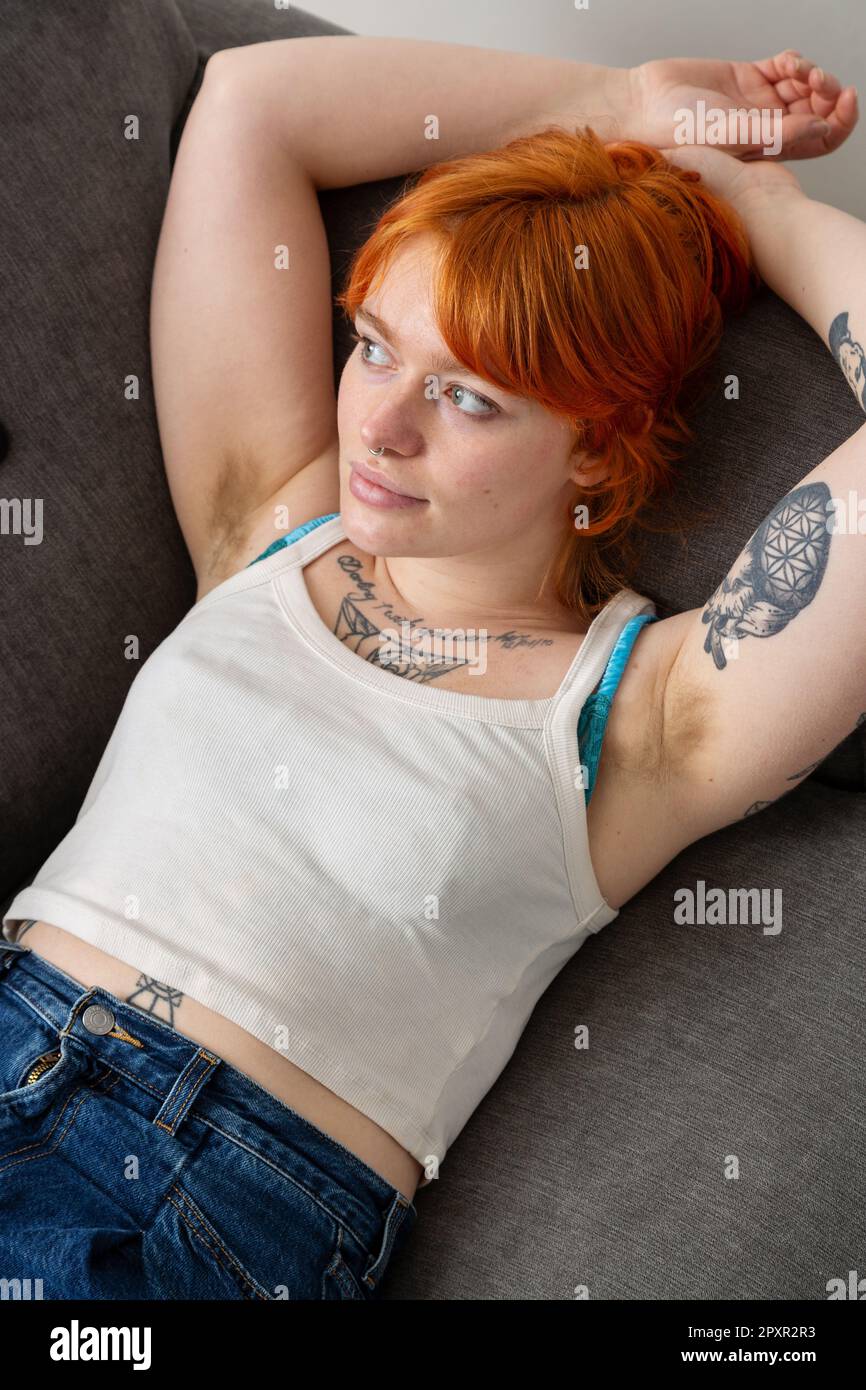 Una donna con ascelle pelose sdraiata su un divano con le braccia sopra la testa. Foto Stock