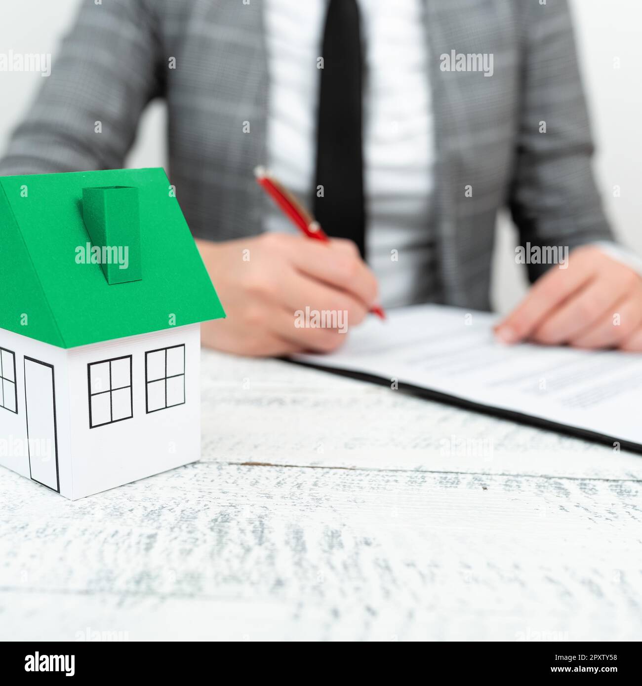 Donna d'affari seduta e scritta nel notebook. Paper house sulla scrivania. Foto Stock