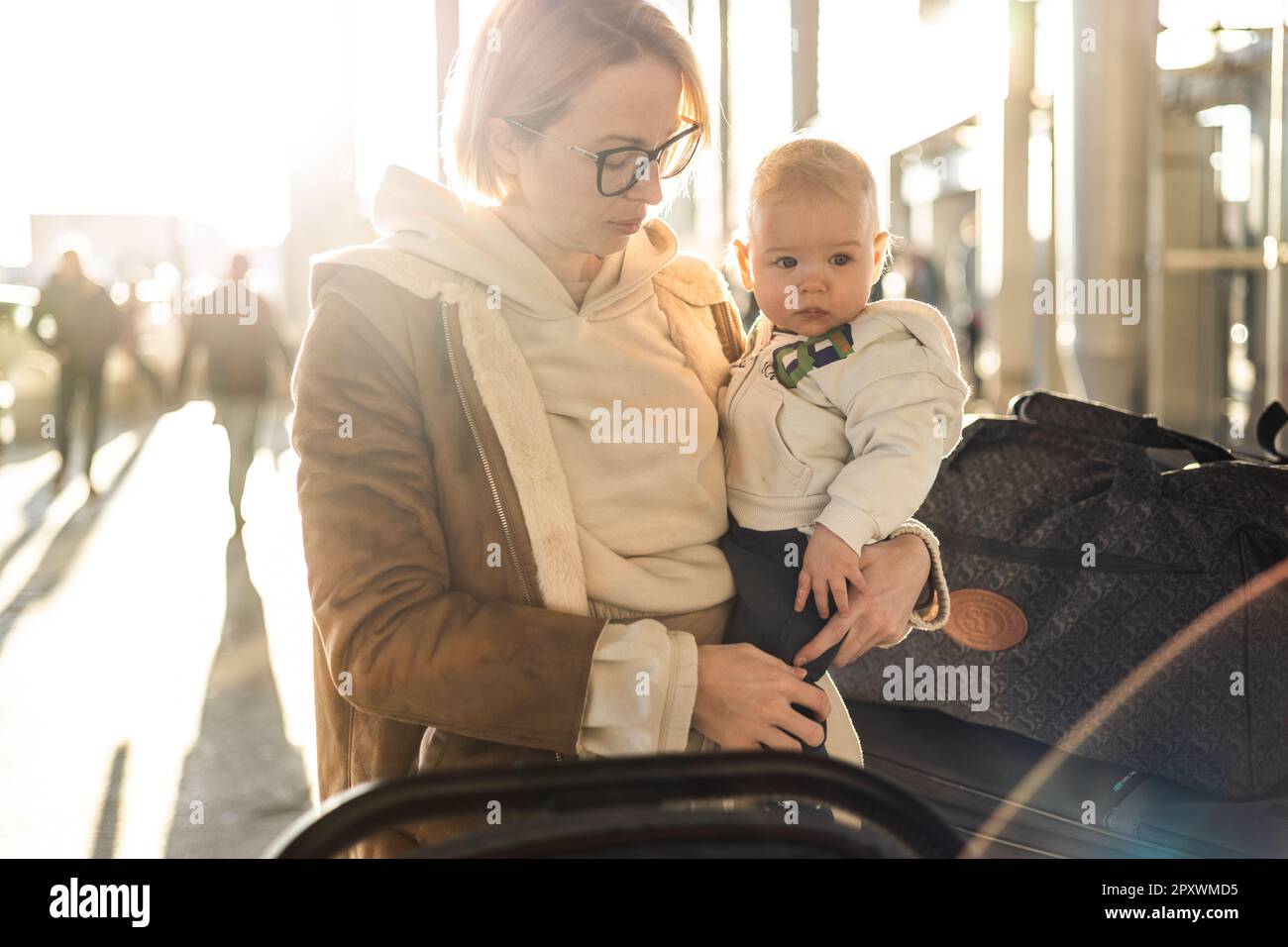 Motherat viaggia con il bambino, camminando, spingendo passeggino e carretto bagagli davanti alla stazione del terminal aeroportuale Foto Stock