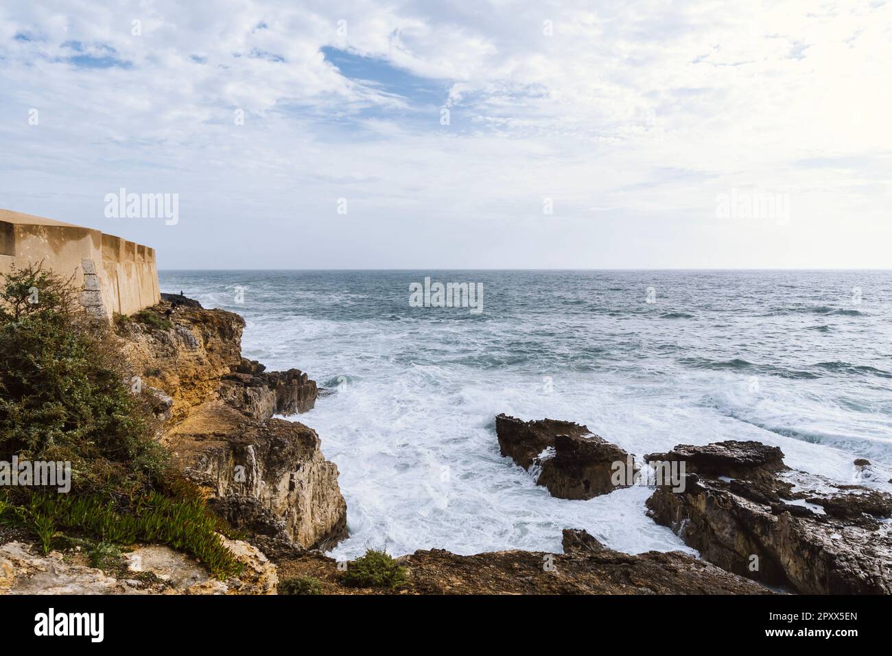 Costa con l'oceano atlantico a Cascais, Portogallo. Onde sulla riva e colline rocciose Foto Stock