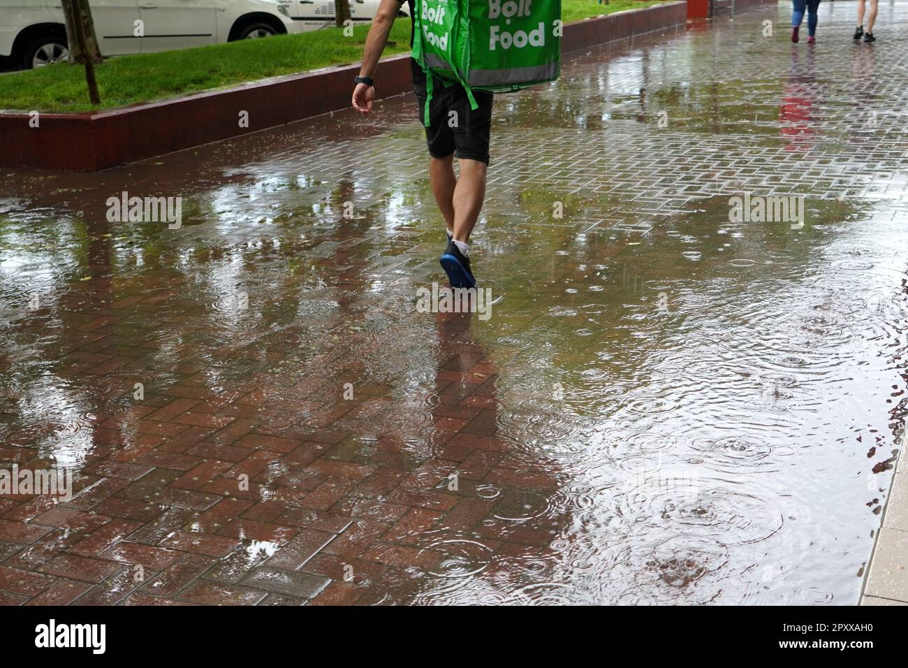 Consegna di cibo uomo da bolt società che cammina attraverso piovere dopo forte pioggia su un marciapiede pavimentato a Bucarest, Romania il 28 maggio 2022 Foto Stock