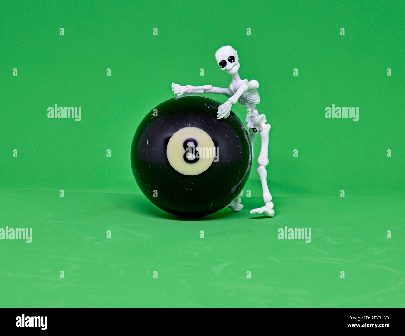 Primo piano di una palla da biliardo o da biliardo numero 8. Su sfondo verde come su un tavolo da biliardo. Con uno scheletro dietro la palla 8. Foto Stock