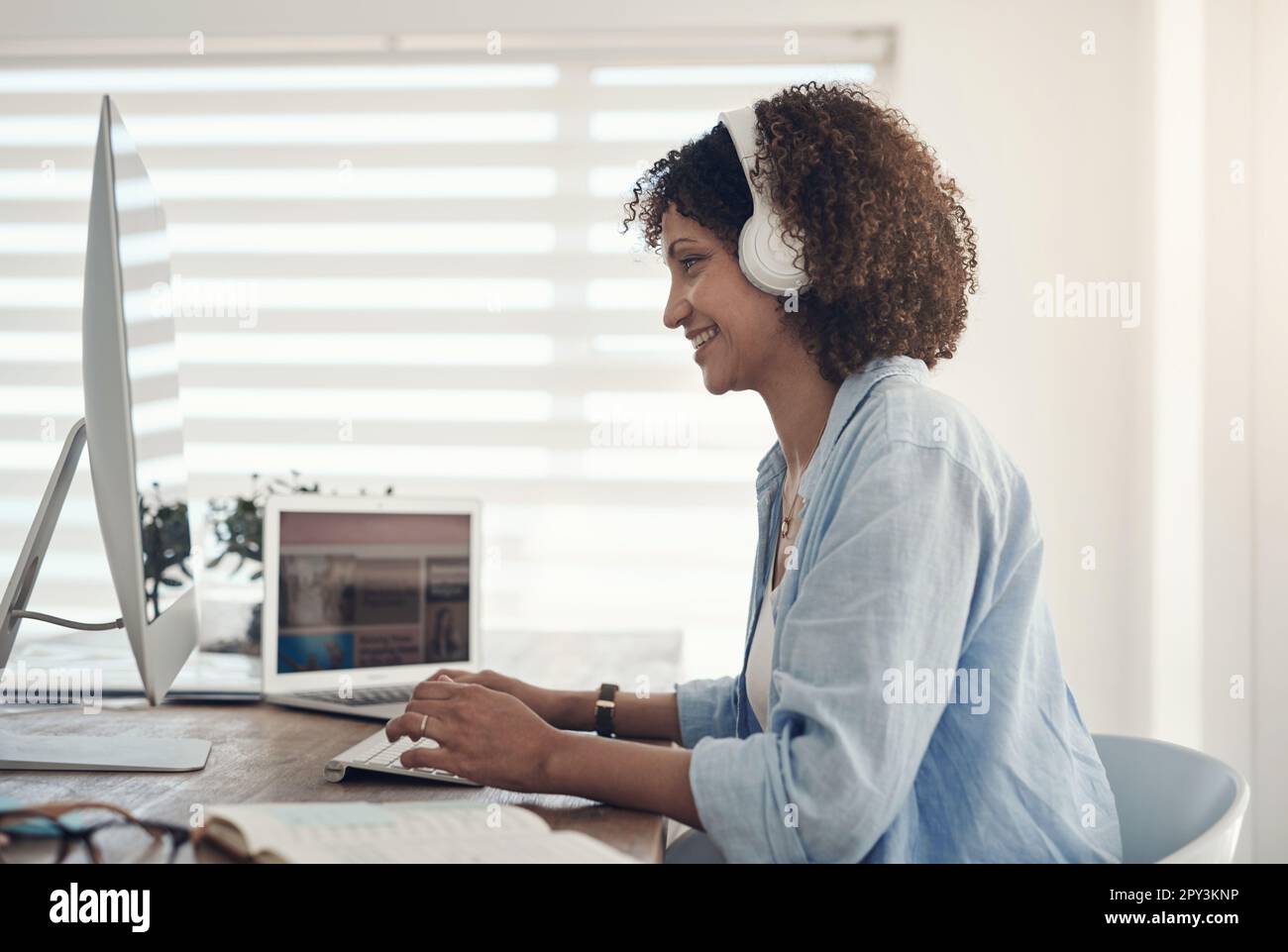 Questo buon umore è stato sponsorizzato dalla musica. una giovane donna attraente che si siede da sola a casa e usa il suo computer mentre indossa le cuffie. Foto Stock