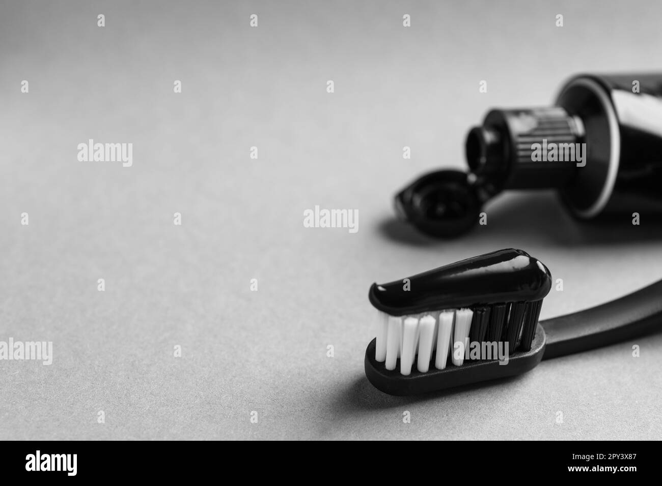 Spazzola con dentifricio al carbone su sfondo grigio chiaro, primo piano. Spazio per il testo Foto Stock