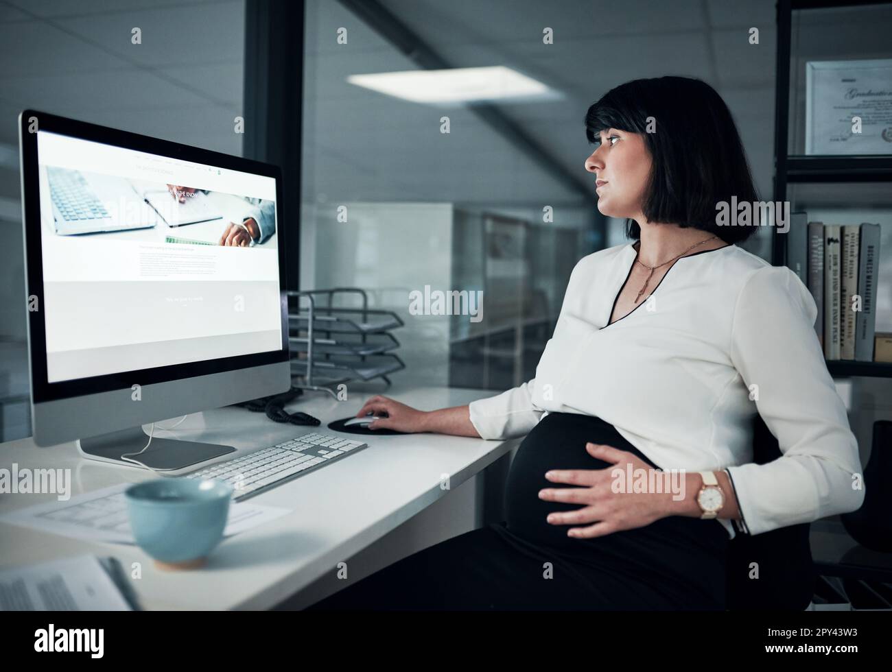 La gravidanza non sarà la ragione per cui mi rallenta. una donna d'affari incinta attraente seduta nel suo ufficio e usando il suo computer mentre tiene il suo pancino. Foto Stock