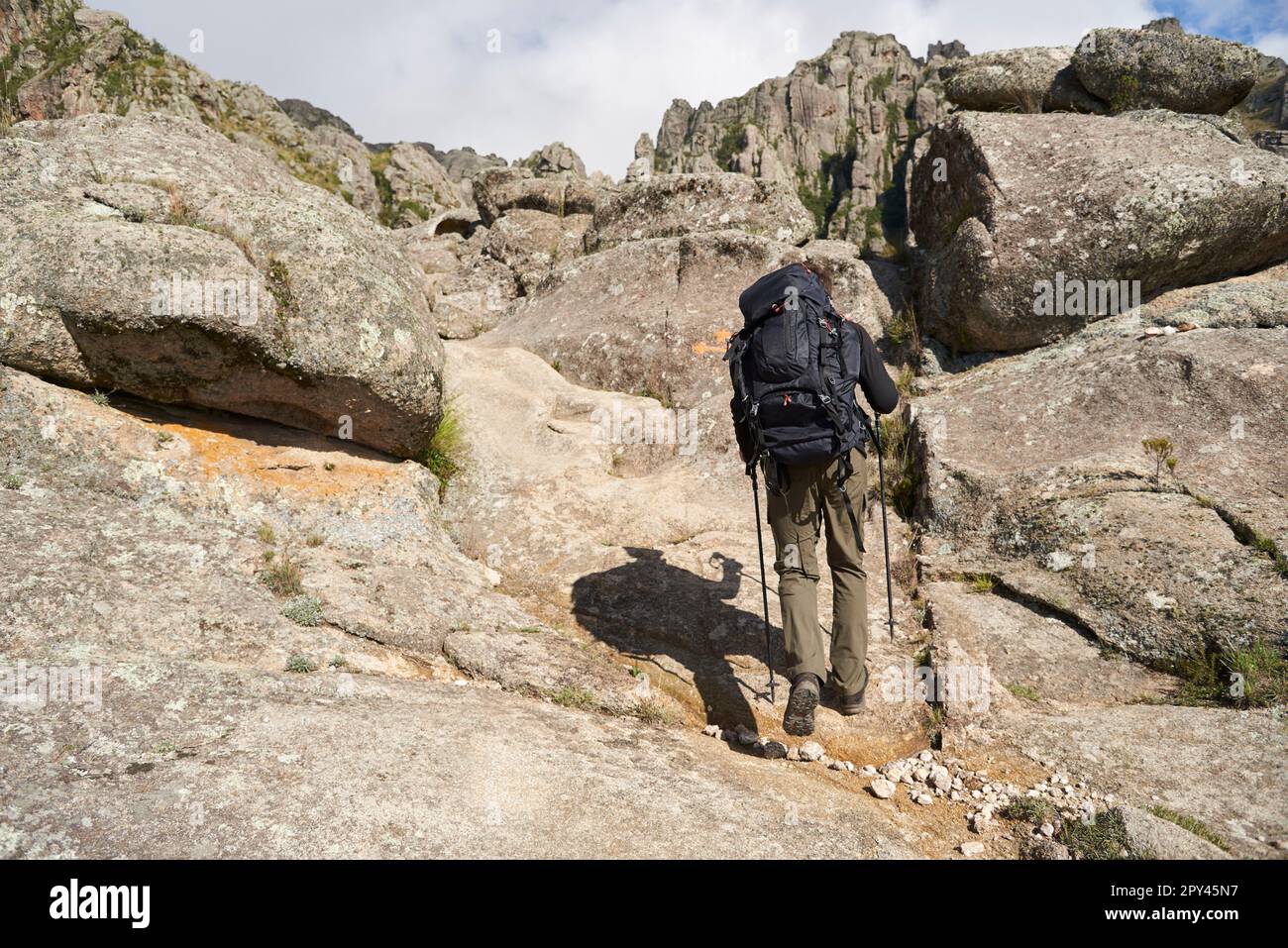 Alpinista irriconoscibile che percorre un sentiero tra un paesaggio roccioso di montagna a Los Gigantes, Cordoba, Argentina, una famosa destinazione turistica. Foto Stock