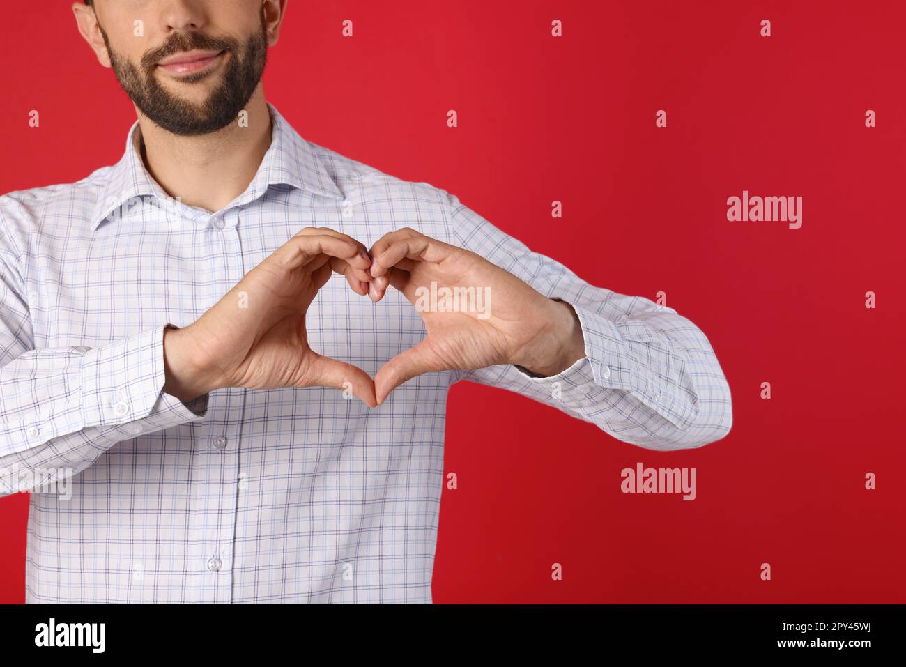 Uomo che fa cuore con le mani su sfondo rosso, primo piano Foto Stock