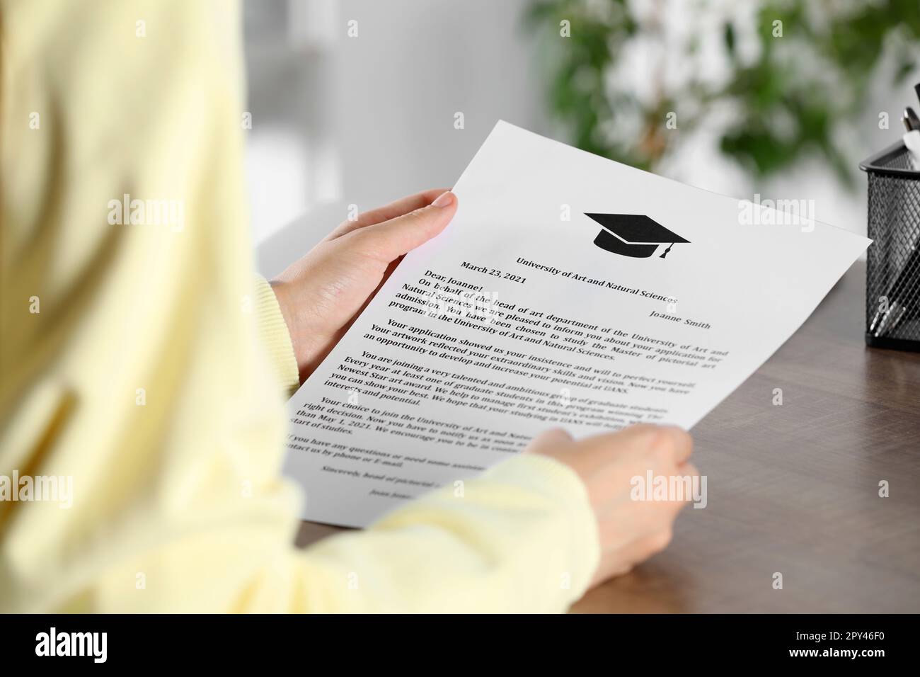 Studente con lettera di accettazione da parte dell'università a tavola di legno al coperto, primo piano Foto Stock