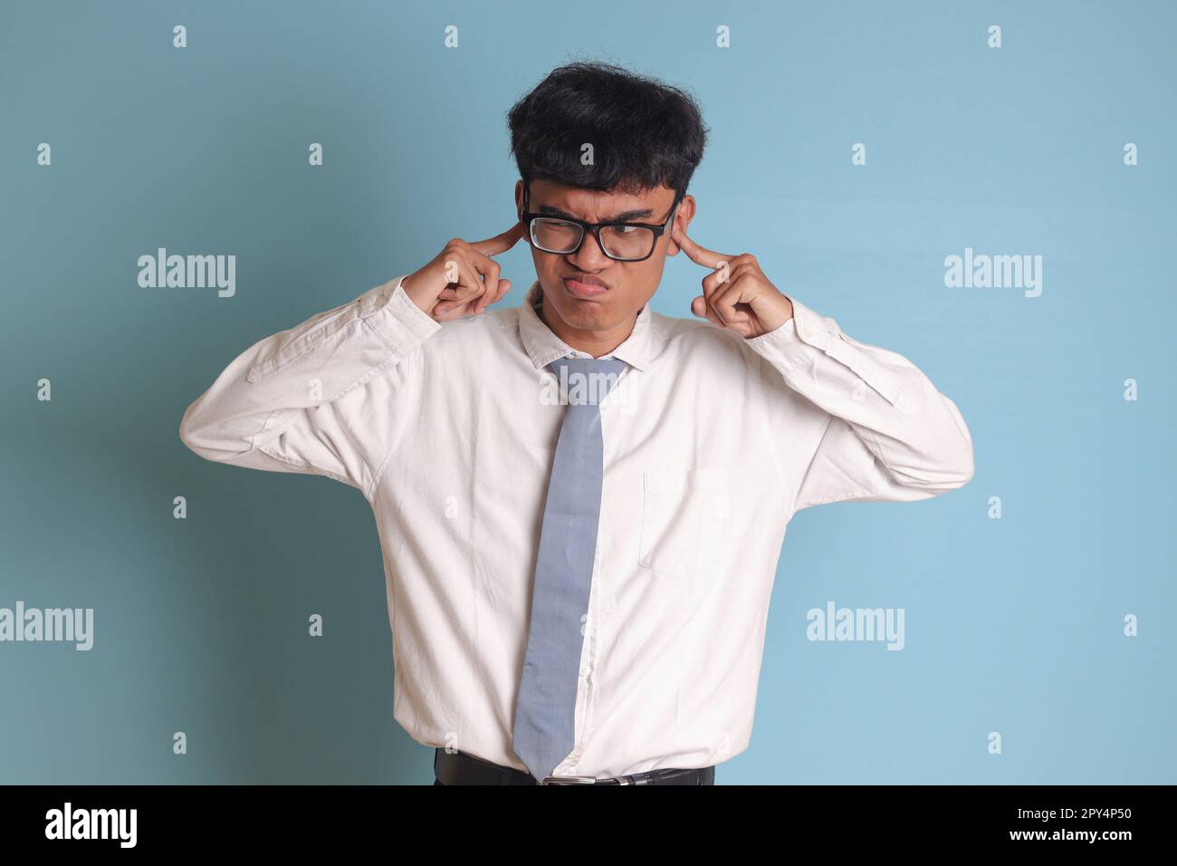 Studente indonesiano di scuola superiore che indossa una maglia bianca uniforme con cravatta grigia che copre le orecchie con le dita, cercando di evitare suoni o voci. Foto Stock