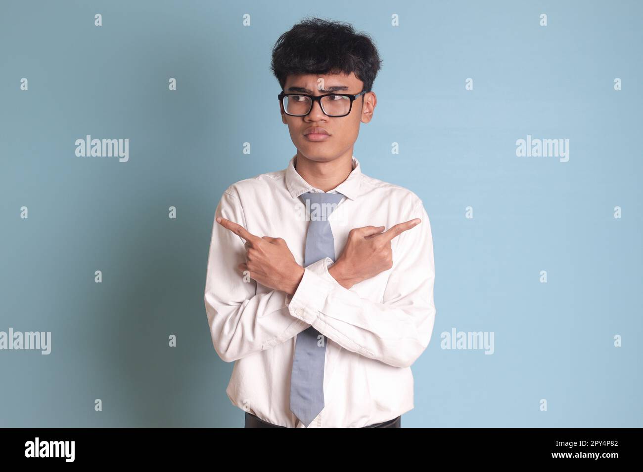 Confuso studente di scuola superiore indossando uniforme camicia bianca con cravatta grigia con mani incrociate, puntando lateralmente, facendo la scelta, scegliendo tra t Foto Stock