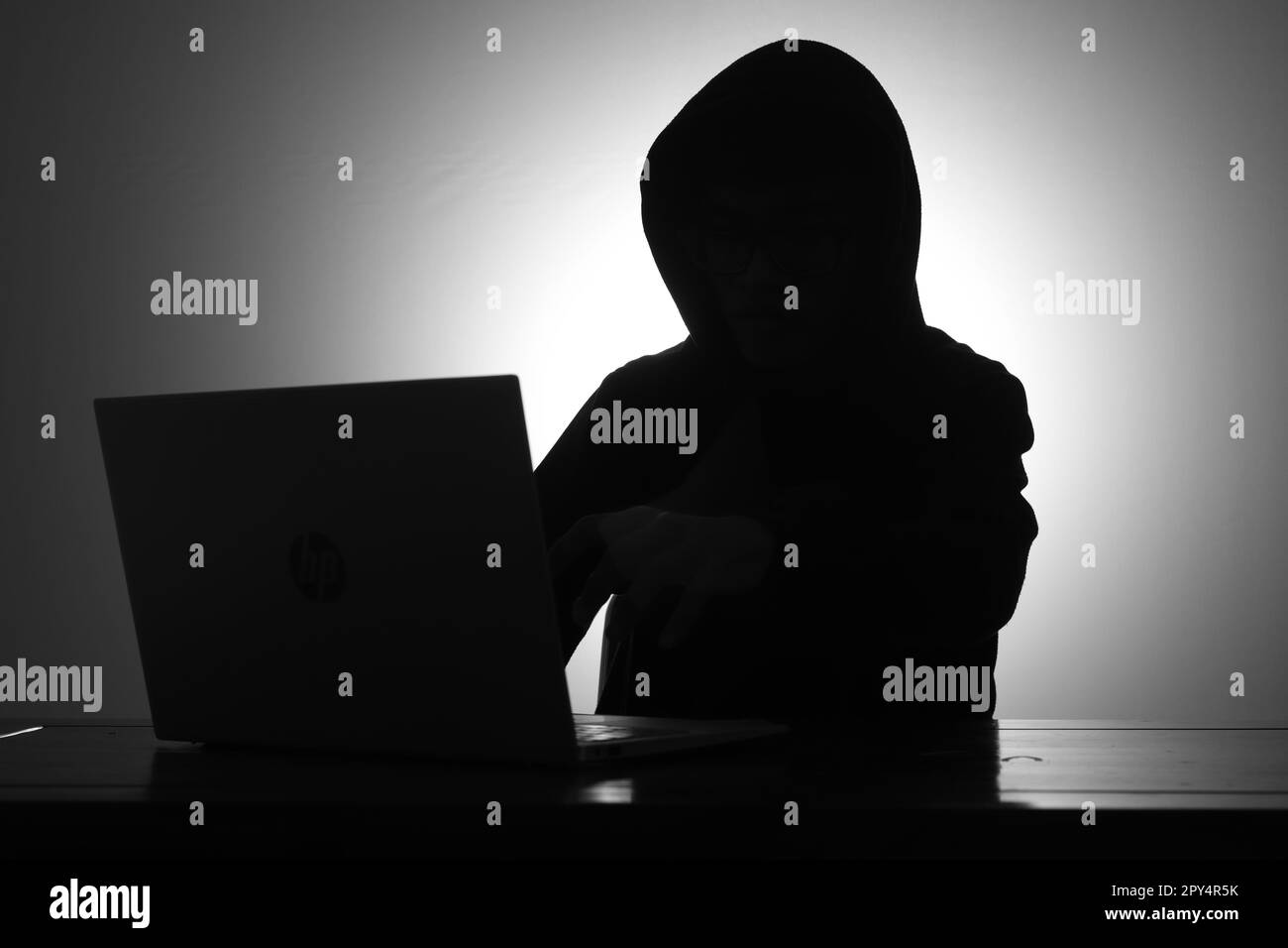 Misterioso uomo che indossa una felpa nera con cappuccio e tiene la carta di credito nella stanza buia. Concetto di hacker e sicurezza informatica. Foto Stock