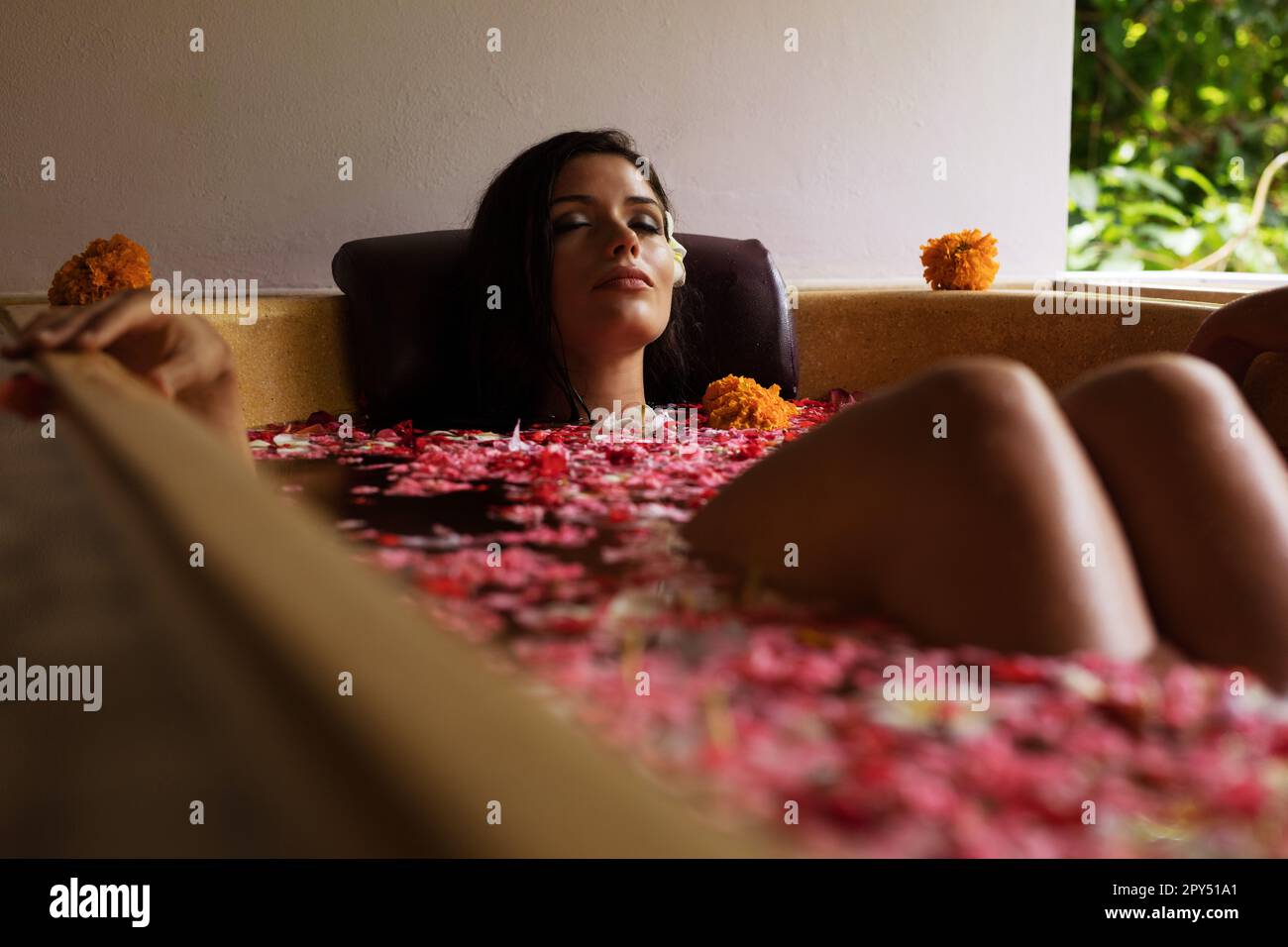 Foto di bella giovane donna in vasca da bagno con petali di fiore. Donne che si rilassano nella vasca da bagno presso un centro benessere. Foto Stock