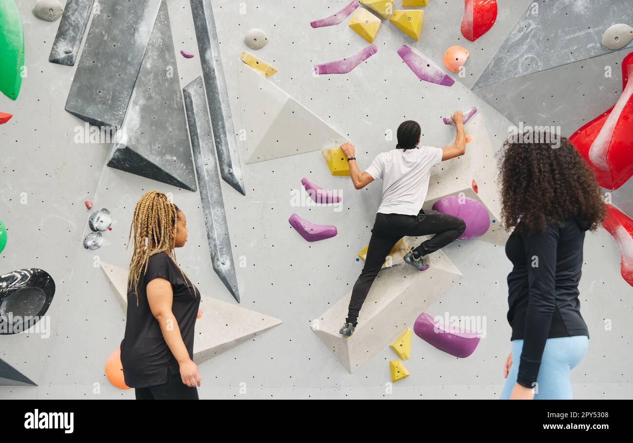Gruppo multiculturale che guarda e incoraggia un amico sulla parete di arrampicata nel centro di attività al coperto Foto Stock