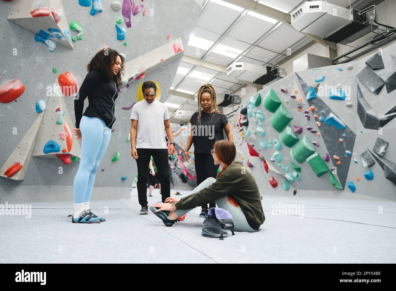 Gruppo multiculturale di amici seduti e indossando scarpe da arrampicata prima di salire a parete nel centro attività al coperto Foto Stock