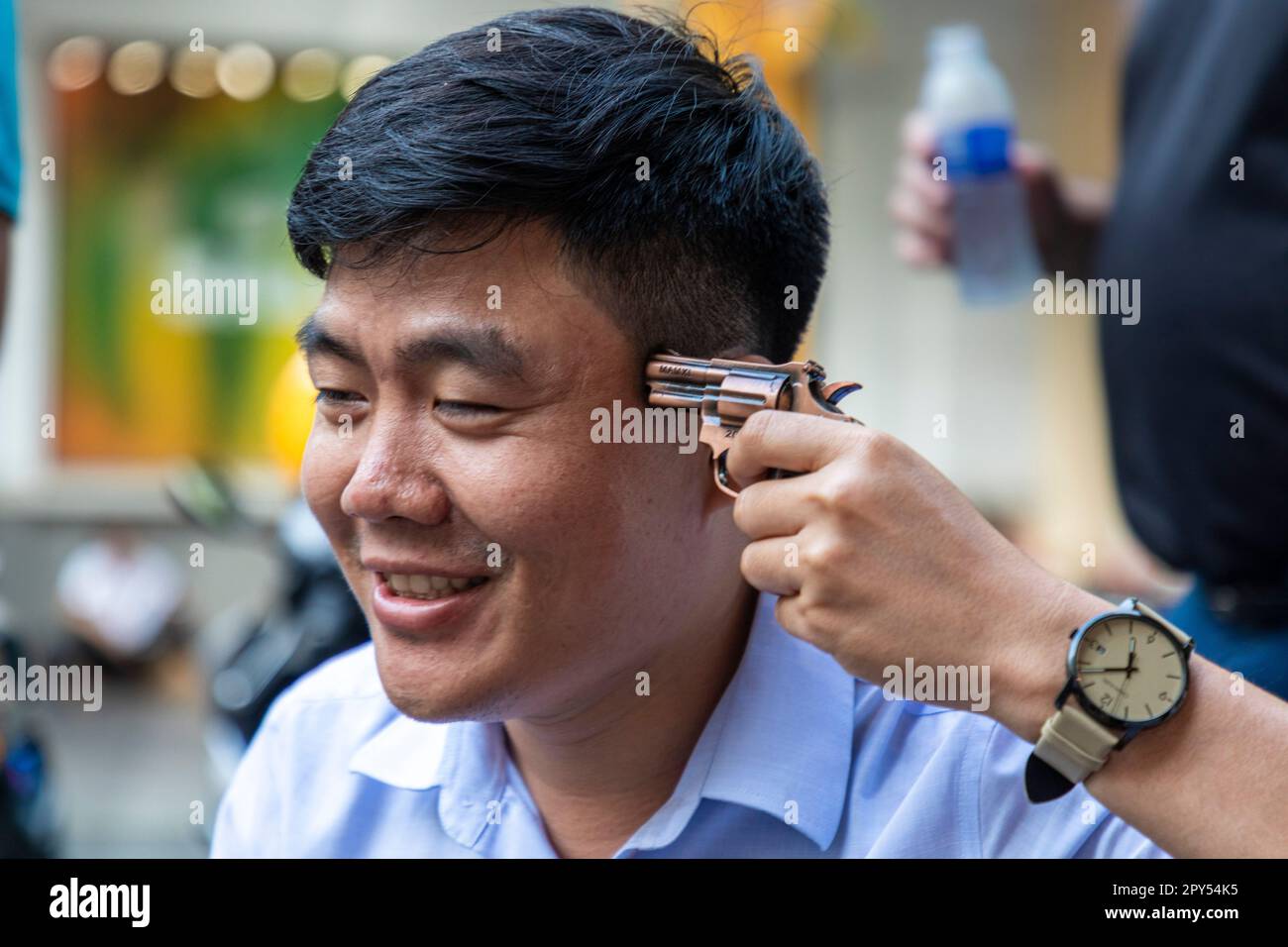 L'uomo vietnamita che posa con un accendisigari a pistola giocattolo puntando alla sua testa, ho Chi Minh City, Vietnam Foto Stock