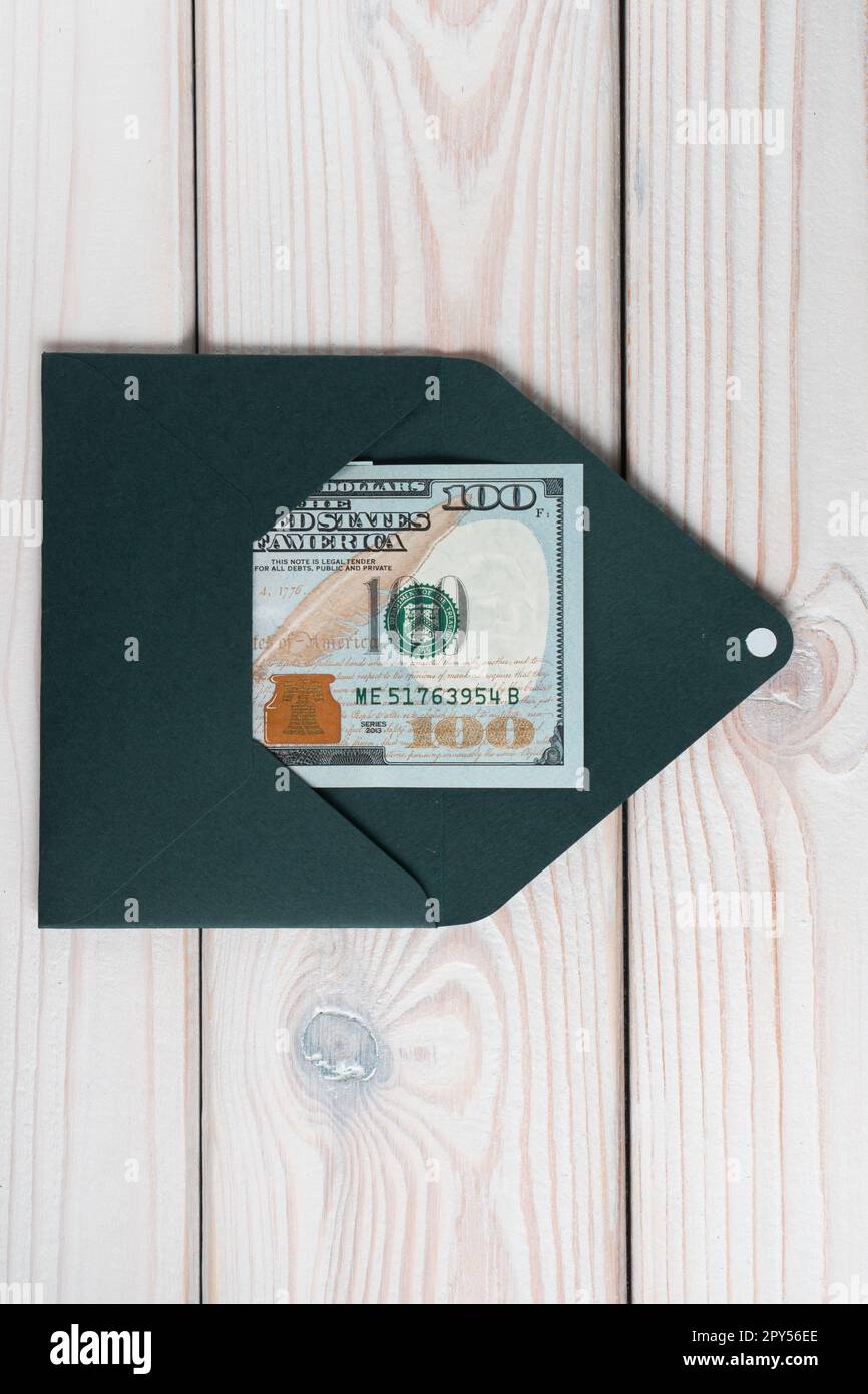 Un piatto di busta verde smeraldo aperta con cento dollari all'interno su un tavolo di legno grigio. Corrispondenza, soldi. Foto Stock