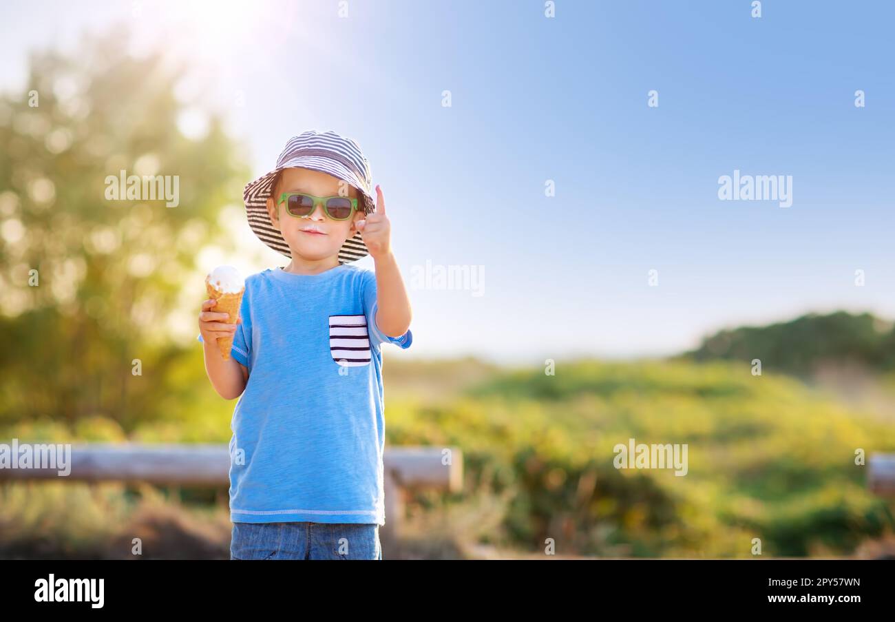 Ragazzo in occhiali da sole in piedi nel parco naturale e mangiare icecream. Foto Stock