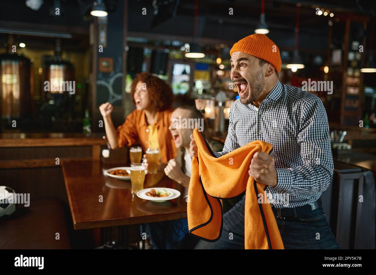 Due ragazzi e una donna al pub che guardano una partita di calcio e bevono birra Foto Stock