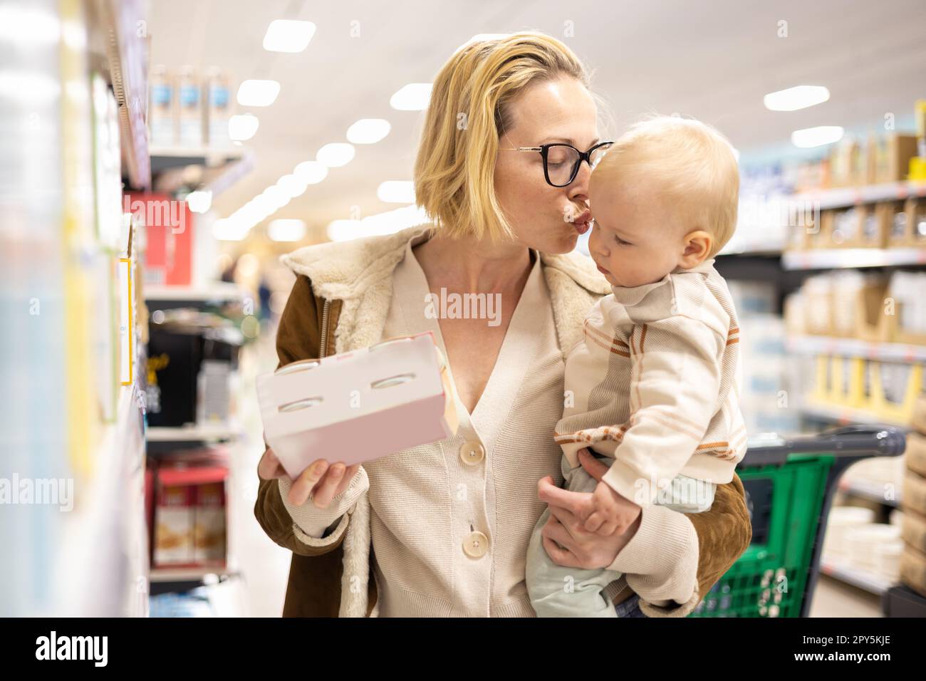 Madre caucasica che fa shopping con il suo bambino neonato che sceglie i prodotti nel grande supermercato. Foto Stock