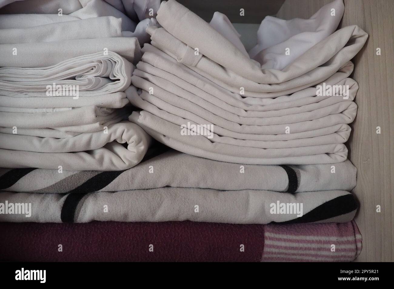 Le lenzuola bianche sono impilate nell'armadio. Contenuto interno di un armadio in lino. Organizzazione familiare. Condizioni igieniche per il sonno. Tessuti e lenzuola in un armadio o guardaroba bianco a metà aperto Foto Stock