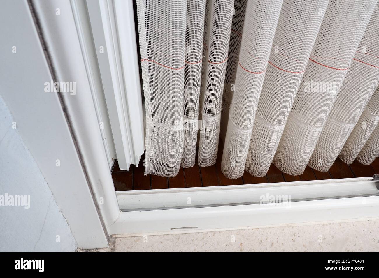 Tende bianche in cotone grossolano o lino fatte di trame di fili sottili. Appartamento interno semplice, compatto ed economico. Decorazione delle finestre in camera. Striscia rossa. Foto Stock