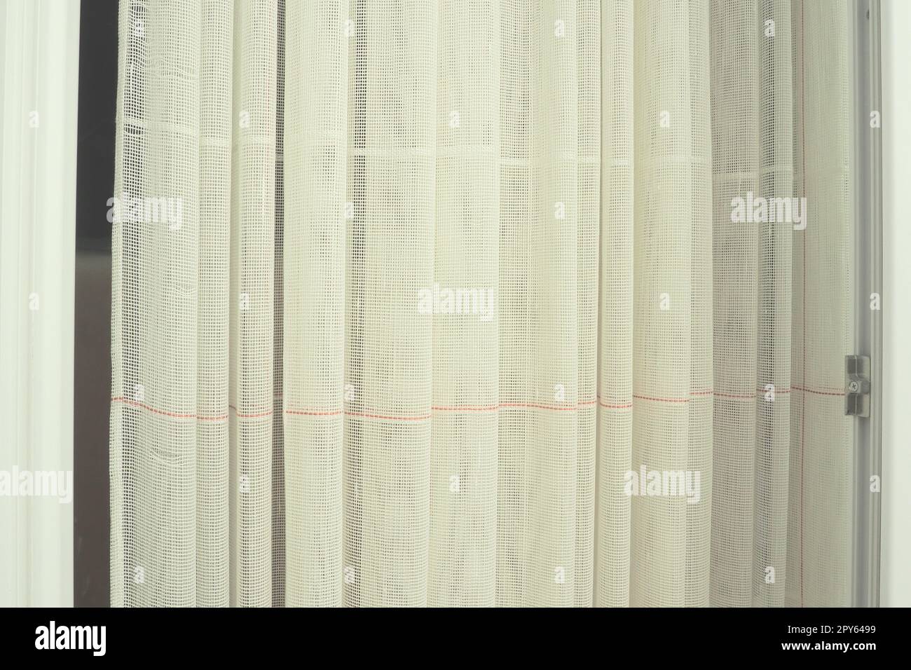 Tende bianche in cotone grossolano o lino fatte di trame di fili sottili. Appartamento interno semplice, compatto ed economico. Decorazione delle finestre in camera. Striscia rossa. Foto Stock