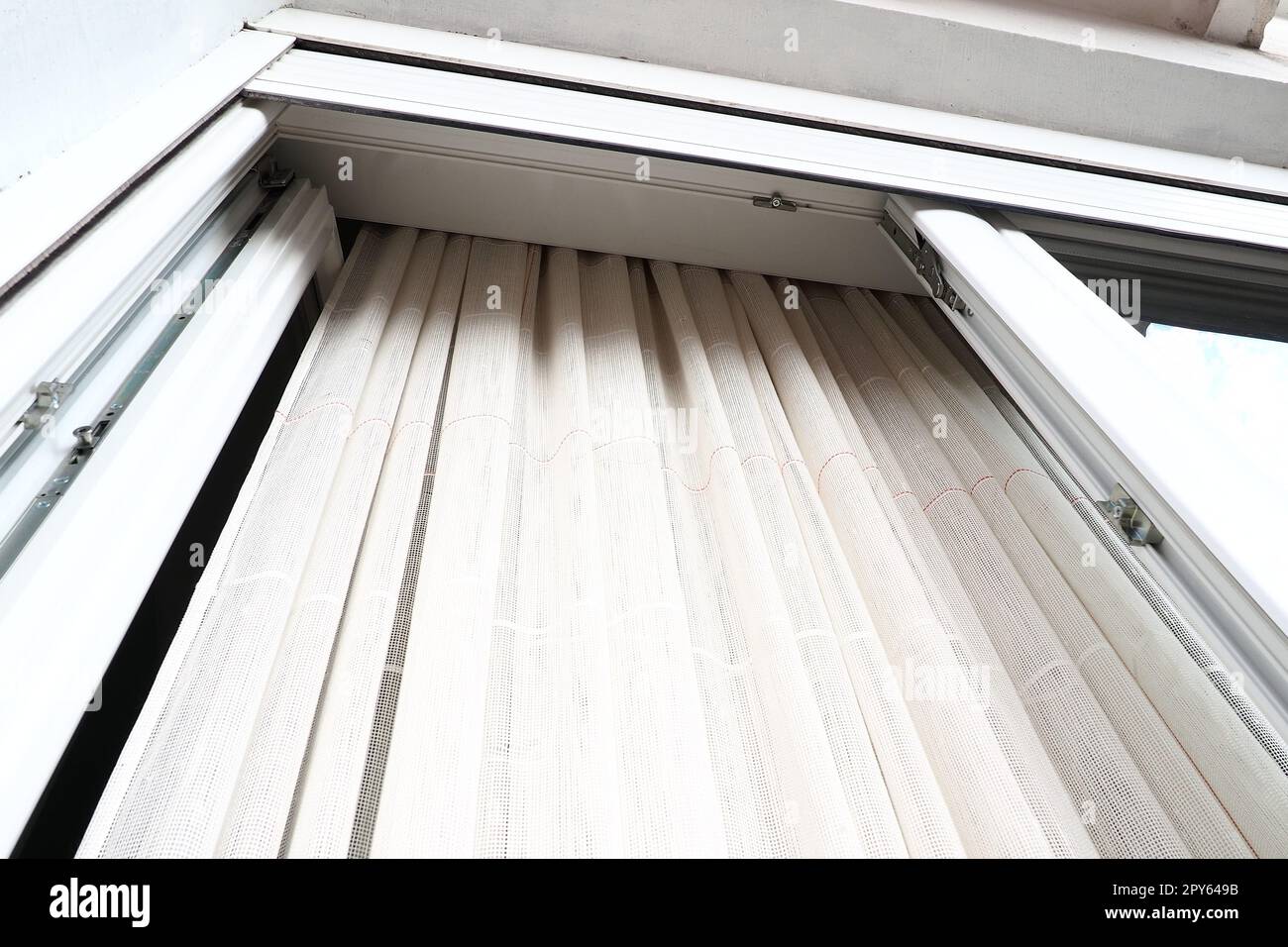 Tende bianche in cotone grossolano o lino fatte di trame di fili sottili. Appartamento interno semplice, compatto ed economico. Decorazione delle finestre in camera. Striscia rossa. Foto Stock