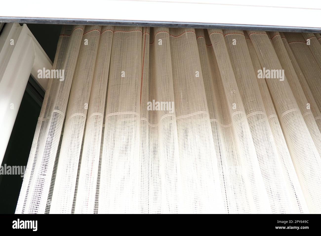 Tende bianche in cotone grossolano o lino fatte di trame di fili sottili. Appartamento interno semplice, compatto ed economico. Decorazione delle finestre in camera. Striscia rossa. Foto Stock