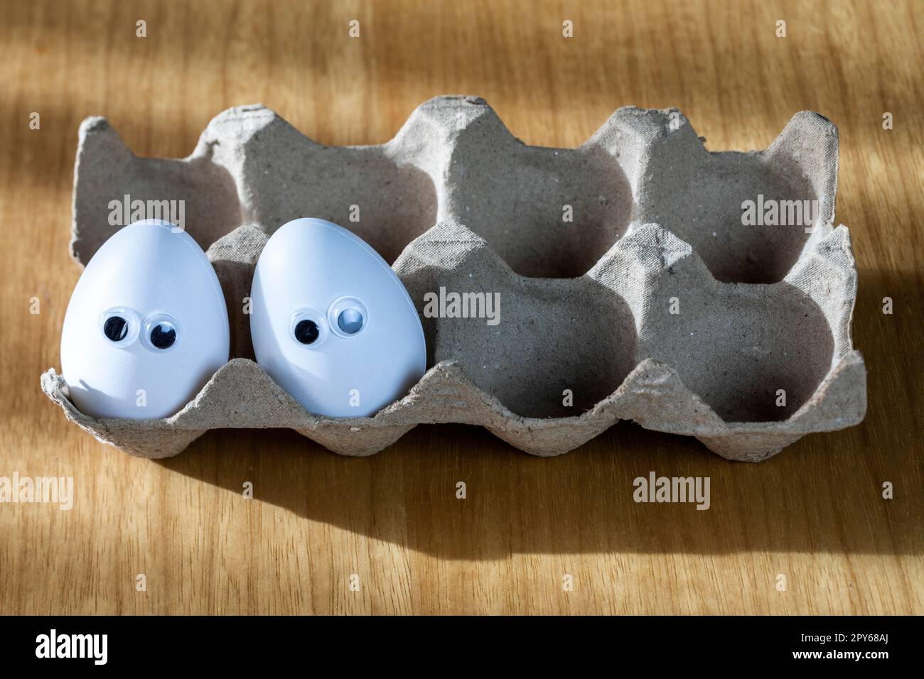 Volti divertenti su uova bianche in scatola di cartone con uova di pollo biologico sul tavolo da cucina primo piano grandi occhi di animazione. umorismo, cibo e vacanza di pasqua concetto. Foto Stock