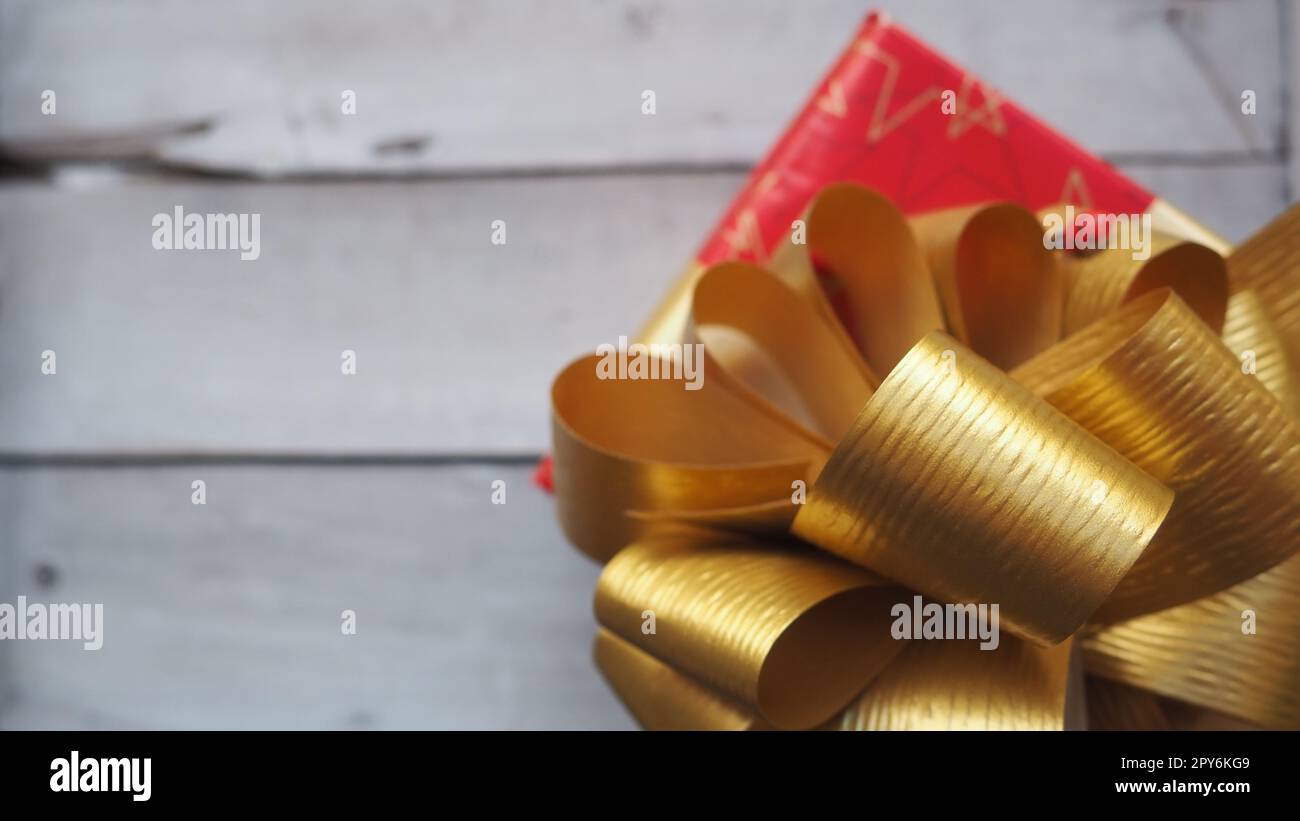 Confezione regalo rossa con un grande arco dorato su sfondo di legno dipinto con vernice bianca. Regalo per Natale, Capodanno, compleanno, festa della mamma, matrimonio, San Valentino. Bella decorazione festiva Foto Stock