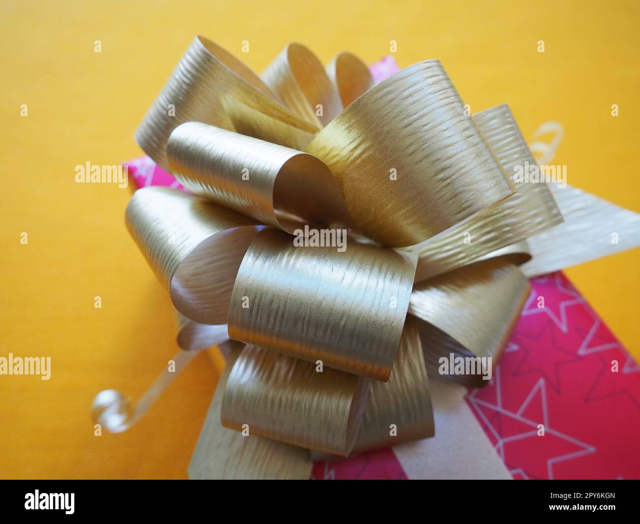 Confezione regalo rossa rosa con un grande fiocco dorato su sfondo giallo ocra. Regalo per Natale, Capodanno, compleanno, festa della mamma, matrimonio, San Valentino. Bella decorazione festiva. Regala regali. Foto Stock