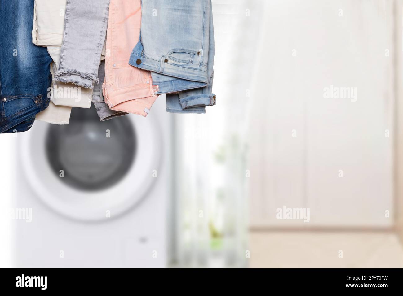 Collezione appesa di vari pantaloni in denim femminili o pantaloni colorati davanti a uno sfondo astratto e sfocato del bagno con spazio per le copie. Per il montaggio del display del prodotto. Foto Stock