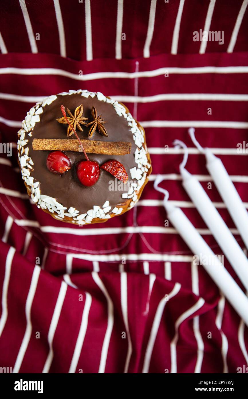 Una tradizionale paska decorata con cioccolato svizzero bianco e fondente e ciliegie, cannella e anice stellato si erge su un grembiule a righe di ciliegia. Pasqua, vista dall'alto. Foto Stock