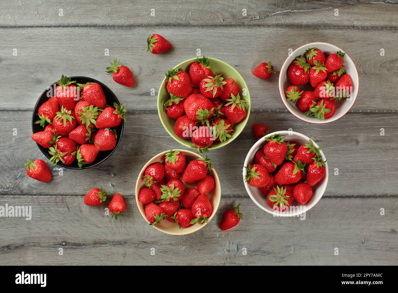 Vista del piano portapaziente, piccole ciotole con fragole, alcuni di loro versato sul legno grigio desk. Foto Stock