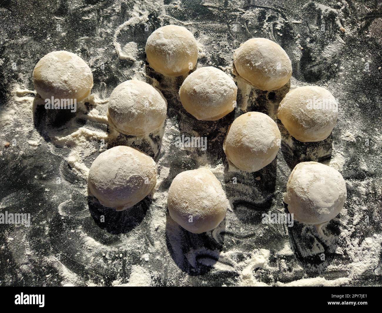Pezzi rotondi di pasta frolla per preparare biscotti o pan di zenzero. Panini crudi o gnocchi con farina sparsi su sfondo nero Foto Stock