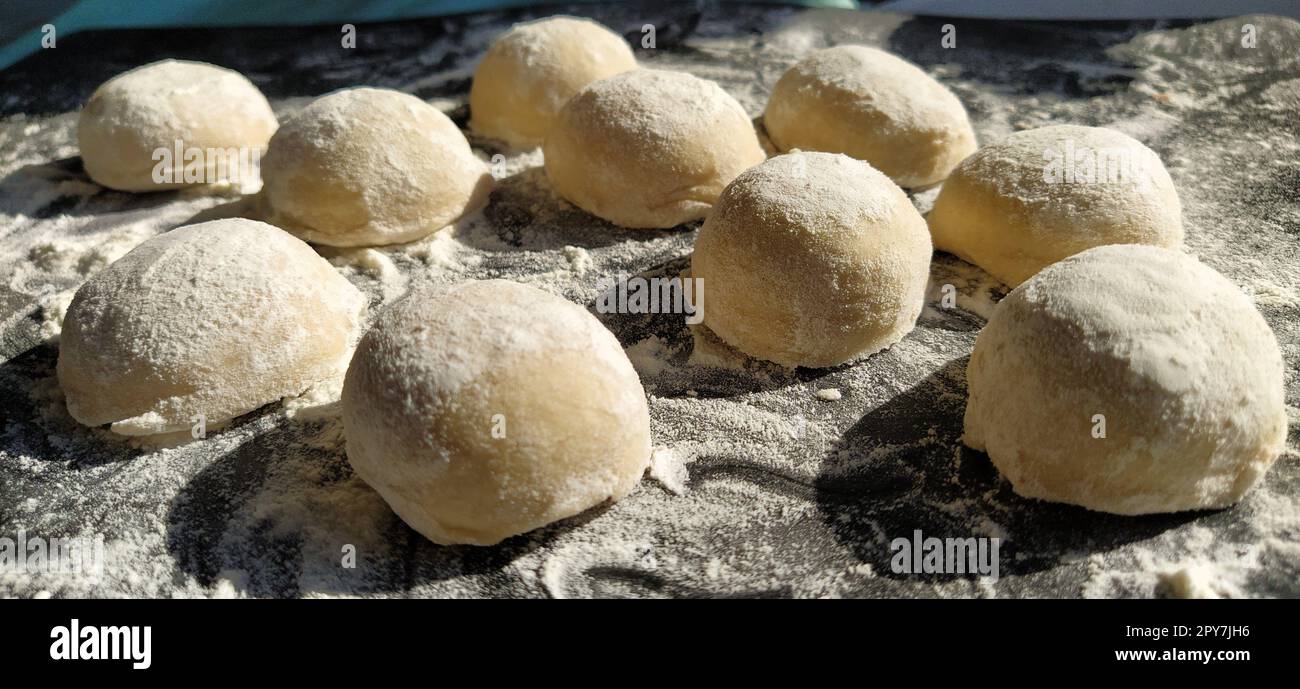 Pezzi rotondi di pasta frolla per preparare biscotti o pan di zenzero. Panini crudi o gnocchi con farina sparsi su sfondo nero Foto Stock