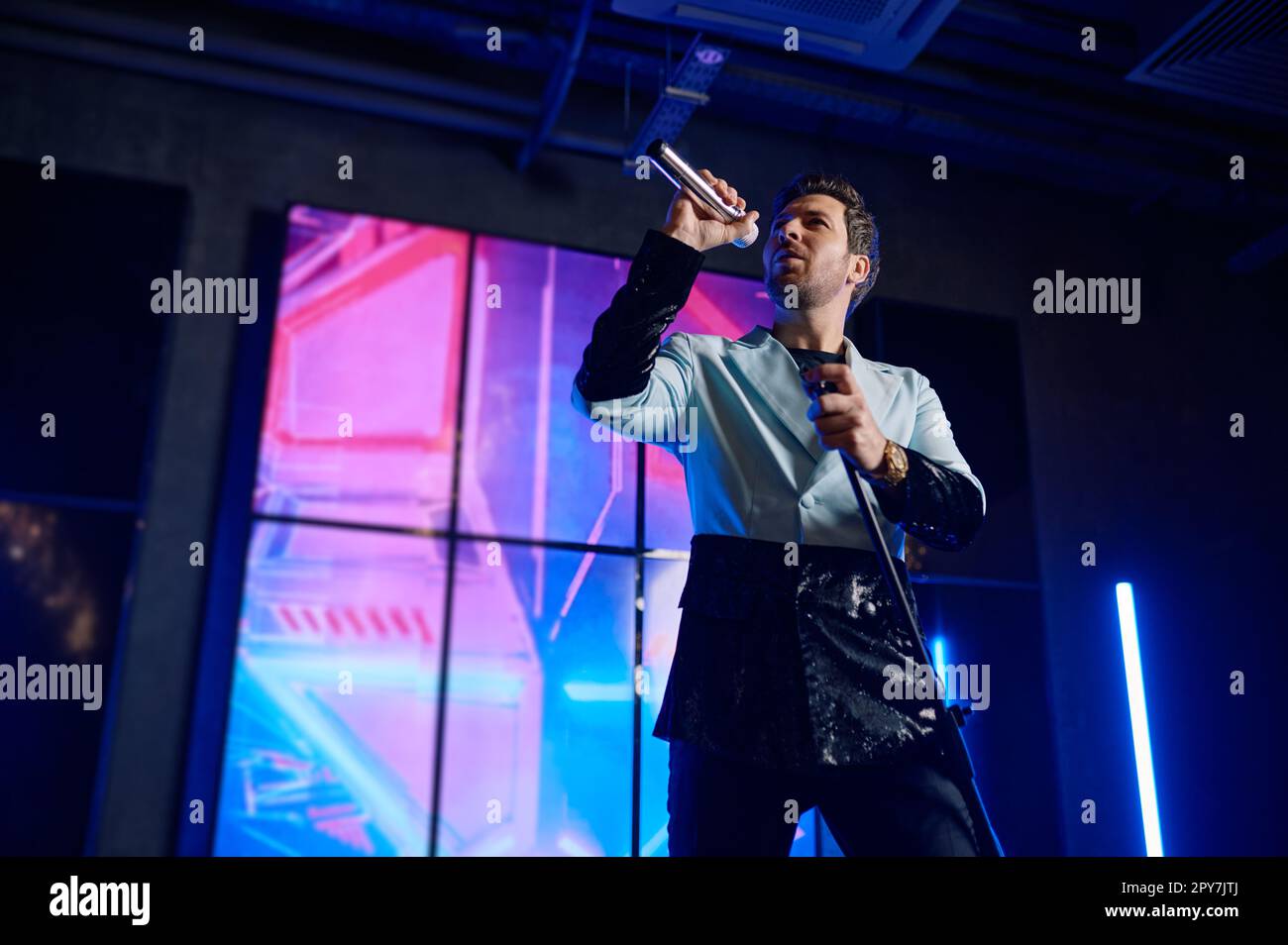 Cantante maschile che tiene il microfono in piedi e che si esibisce sul palco Foto Stock