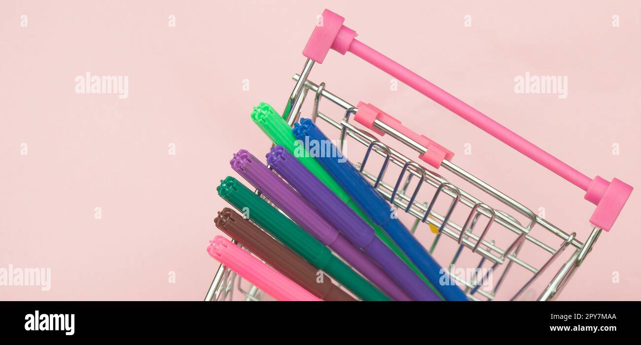 Concetto creativo di apprendimento e creatività con carrello della spesa con pennarelli su sfondo rosa, spazio di copia Foto Stock