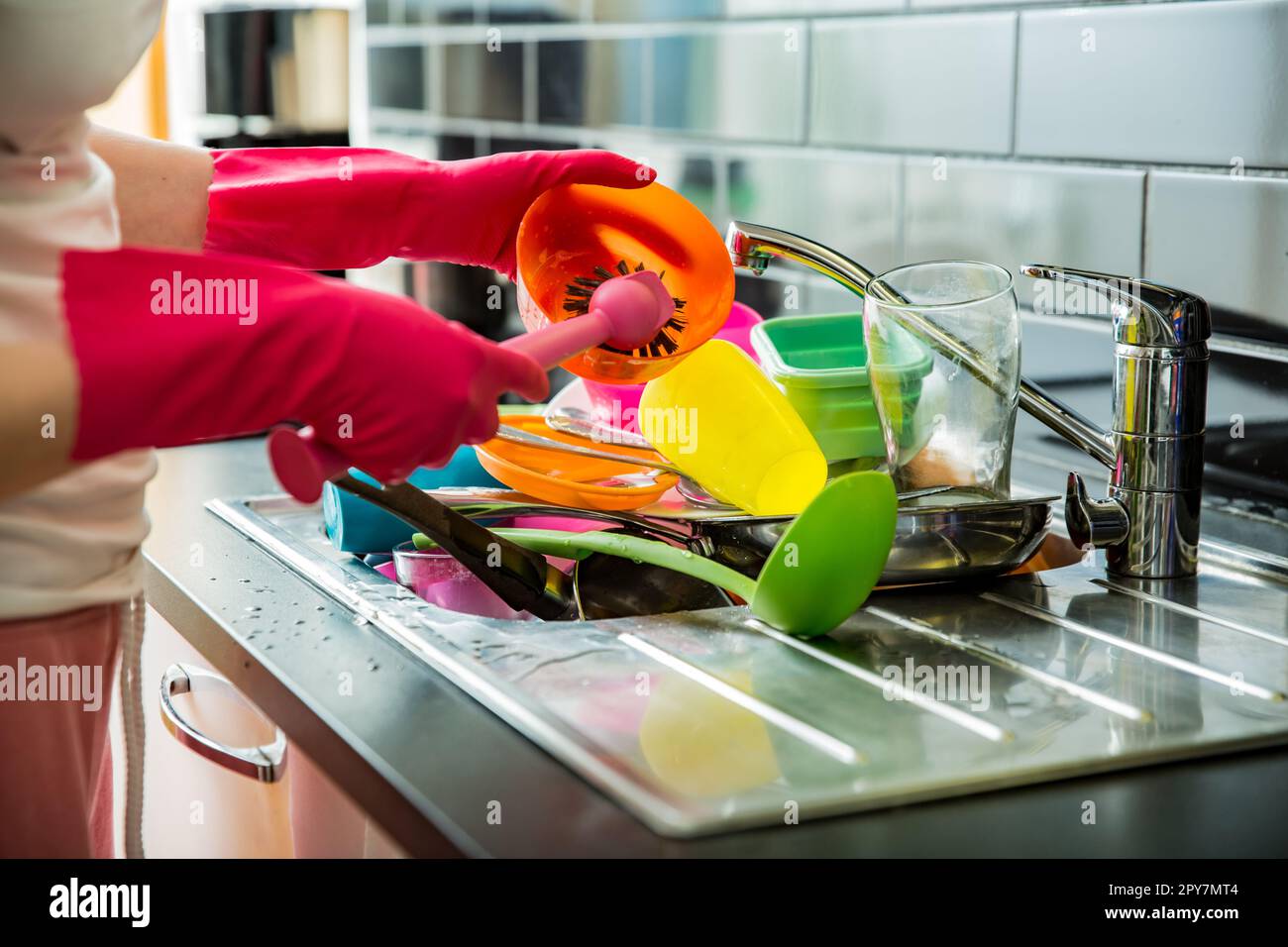Lavandino da cucina pieno di piatti sporchi. Donna in guanti di gomma rosa che fanno i piatti, utilizzando la spazzola. Piano di appoggio di colore scuro in una cucina moderna. Lavori di casa Foto Stock