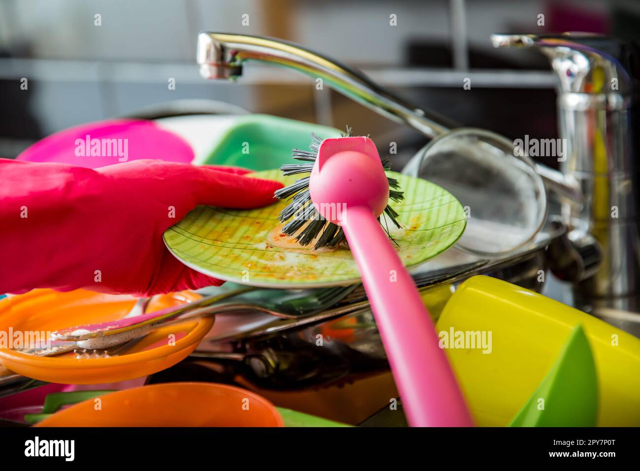 Lavandino da cucina pieno di piatti sporchi. Donna in guanti di gomma rosa che fanno i piatti, utilizzando la spazzola. Piano di appoggio di colore scuro in una cucina moderna. Lavori di casa Foto Stock