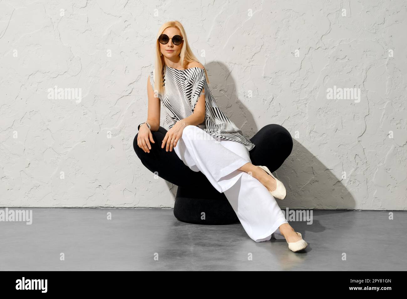 Donna bionda con camicetta e pantaloni larghi lancia la gamba su un'altra gamba Foto Stock