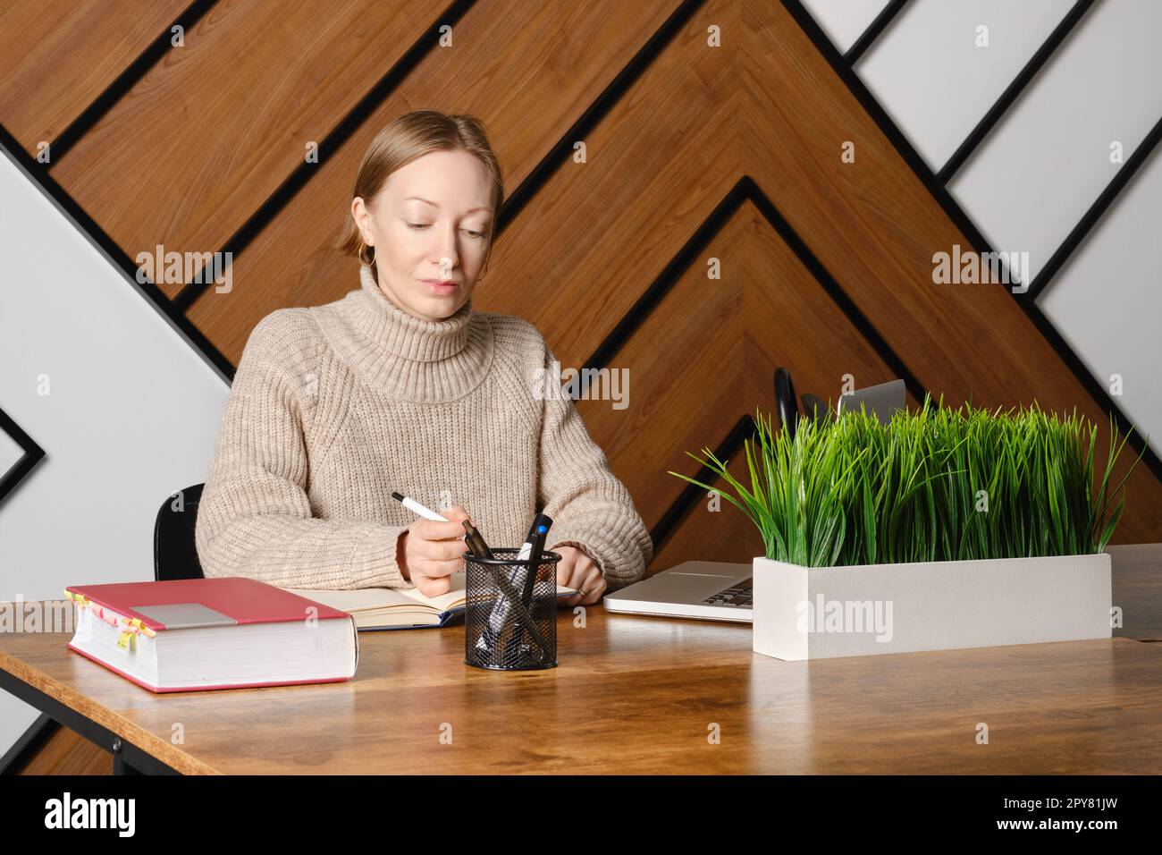 Una donna adulta seria sta lavorando sodo nel co-working e nel prendere appunti in blocco note Foto Stock