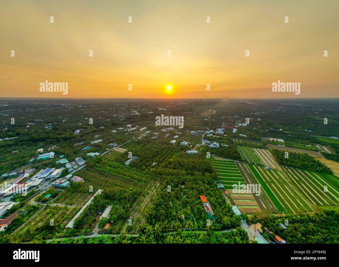 Golden Hour Magic: Tramonto mozzafiato sui campi della provincia di Tien Giang con il fiume sereno e il paesaggio urbano in Vietnam Foto Stock