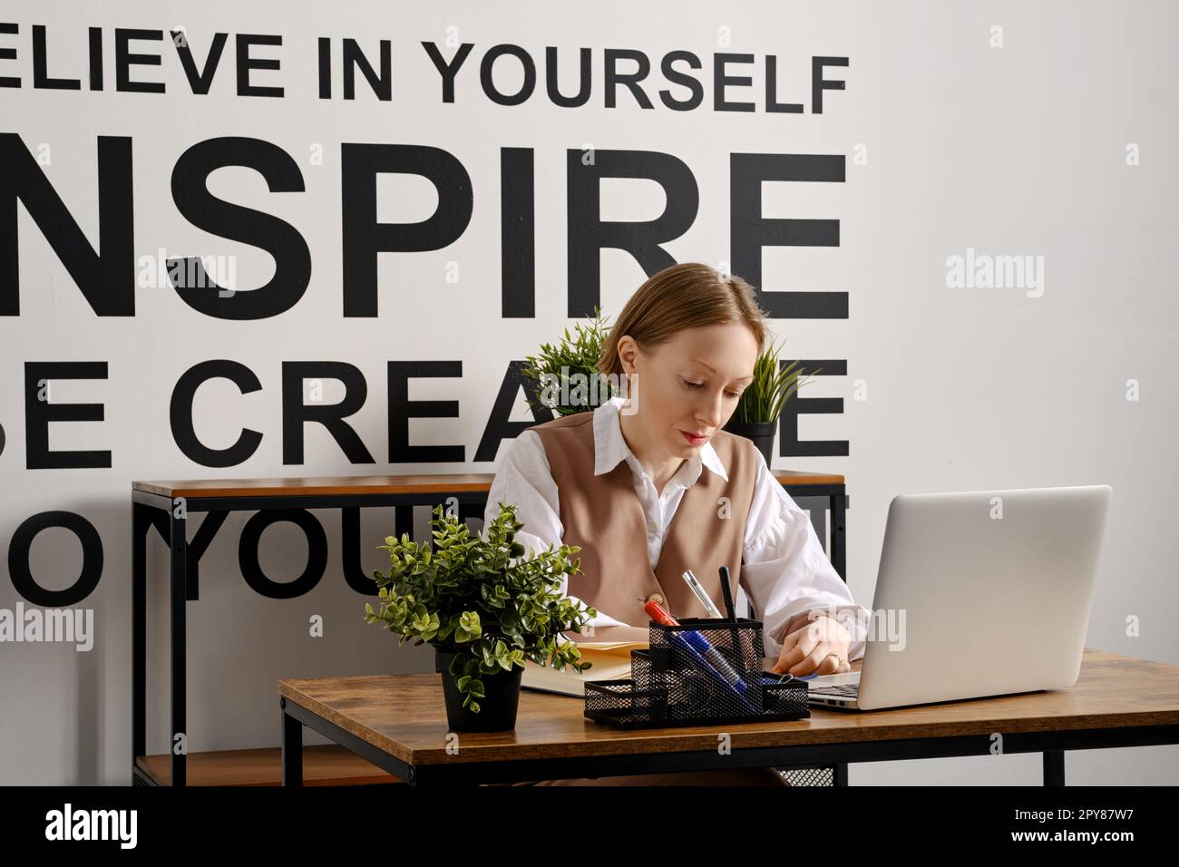 Una donna adulta sta lavorando sodo a un notebook e prende appunti all'ordine del giorno Foto Stock