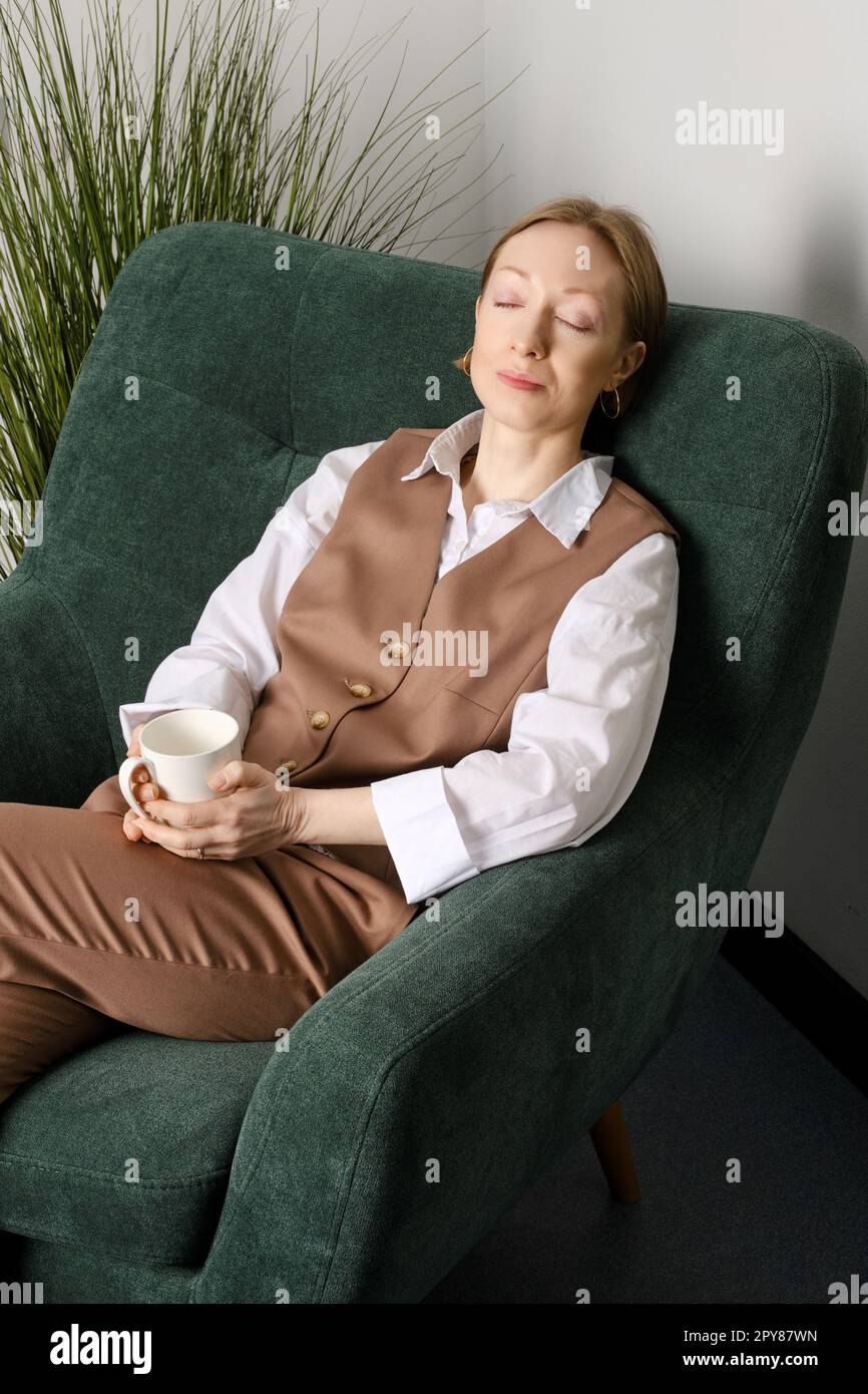 Donna di mezza età che si riposa durante la pausa caffè nella sala ricreativa dell'ufficio Foto Stock