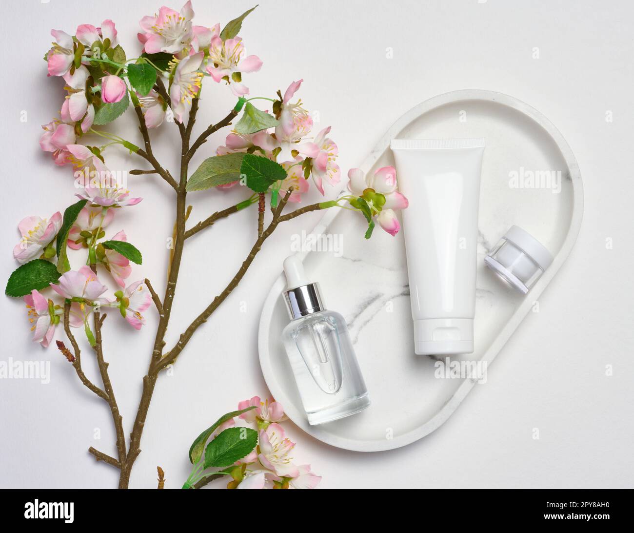 Vasca di plastica bianca, bottiglia di vetro con un contagocce su un supporto di marmo, e un bouquet di ciliegia fiorente su uno sfondo bianco, contenitore cosmetico, vista dall'alto Foto Stock