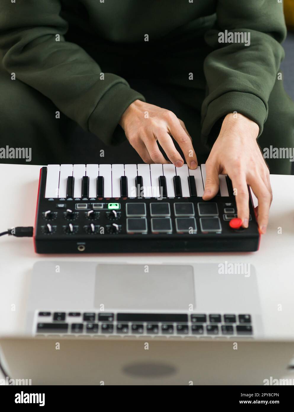 Uomo che registra brani musicali elettronici con tastiera Midi portatile su un computer portatile in studio domestico. Produrre e mixare musica beat e organizzare contenuti audio con dispositivi audio professionali Foto Stock