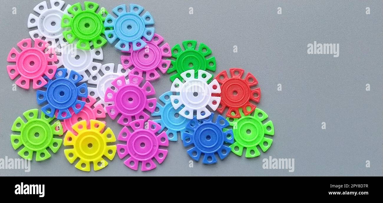 Dettagli multicolore sotto forma di fiocchi di neve del designer di bambini su sfondo grigio. Rosso, giallo, verde, blu, bianco, dischi in plastica rosa per lo sviluppo delle capacità motorie sottili delle dita Foto Stock