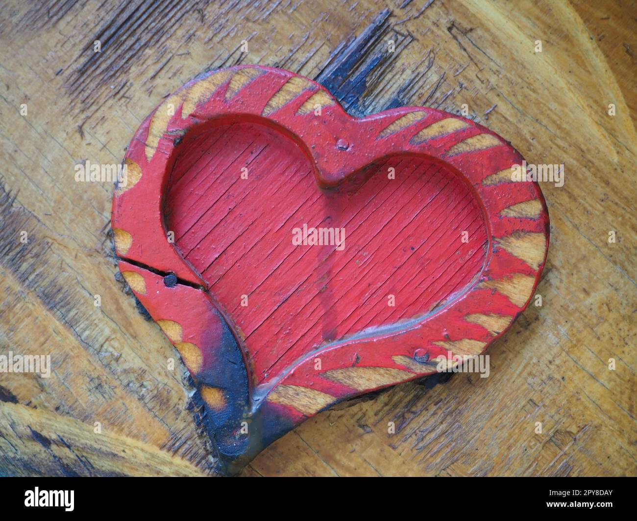 Forma a cuore di falegnameria su una superficie di legno e verniciata di rosso. Un simbolo di amore e fedeltà. Cartolina per le congratulazioni o il riconoscimento di San Valentino. Segni di influenza dell'accensione o dell'umidità. Foto Stock